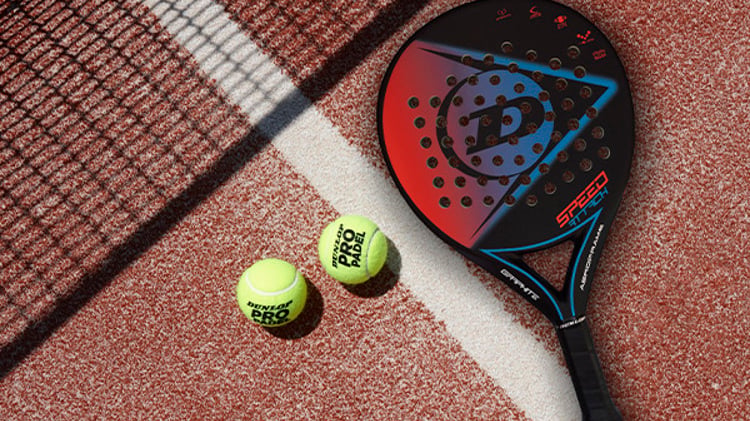 Two padel balls and a Dunlop padel bat on a clay-coloured padel court