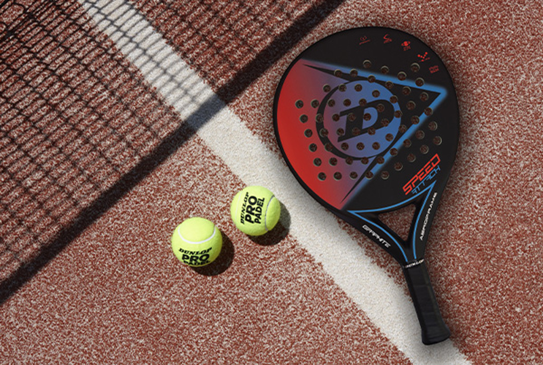 Two padel balls and a Dunlop padel bat on a clay-coloured padel court