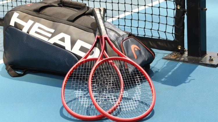 Two tennis rackets laying on top of a head branded bag on a tennis court