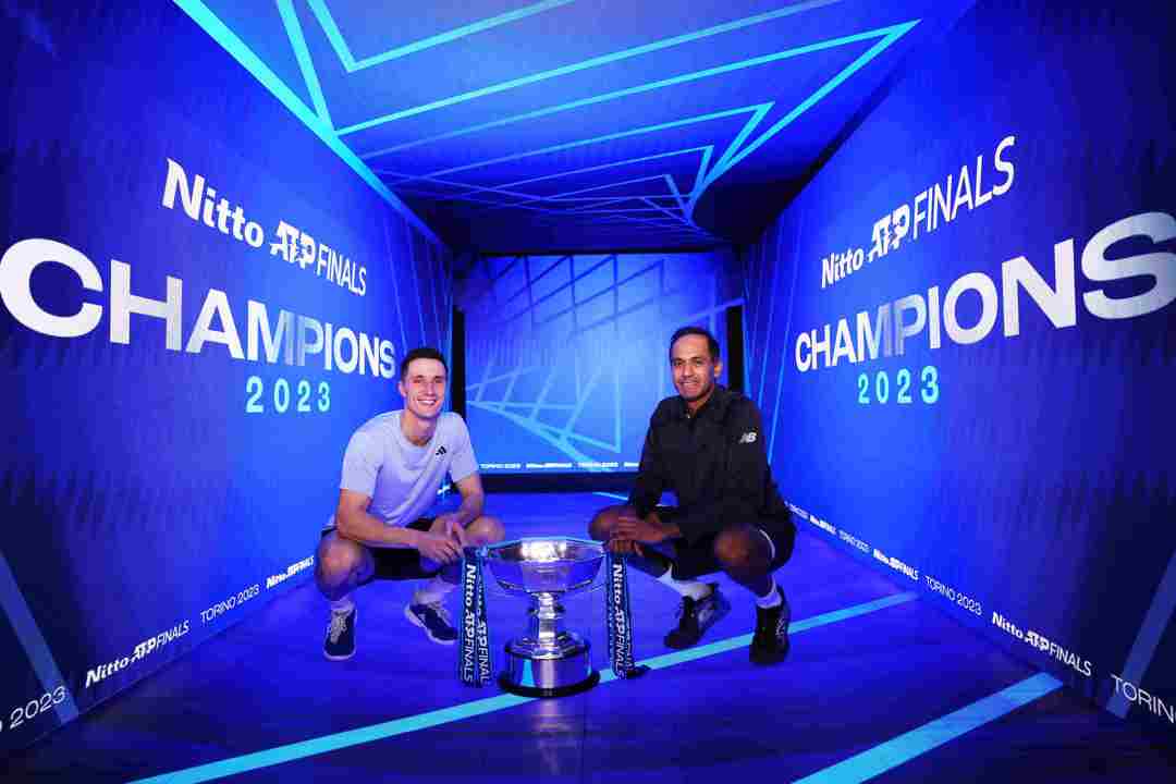 Joe Salisbury and Rajeev Ram crouching down next to the Nitto ATP Finals trophy with a digital screen saying Champions behind them