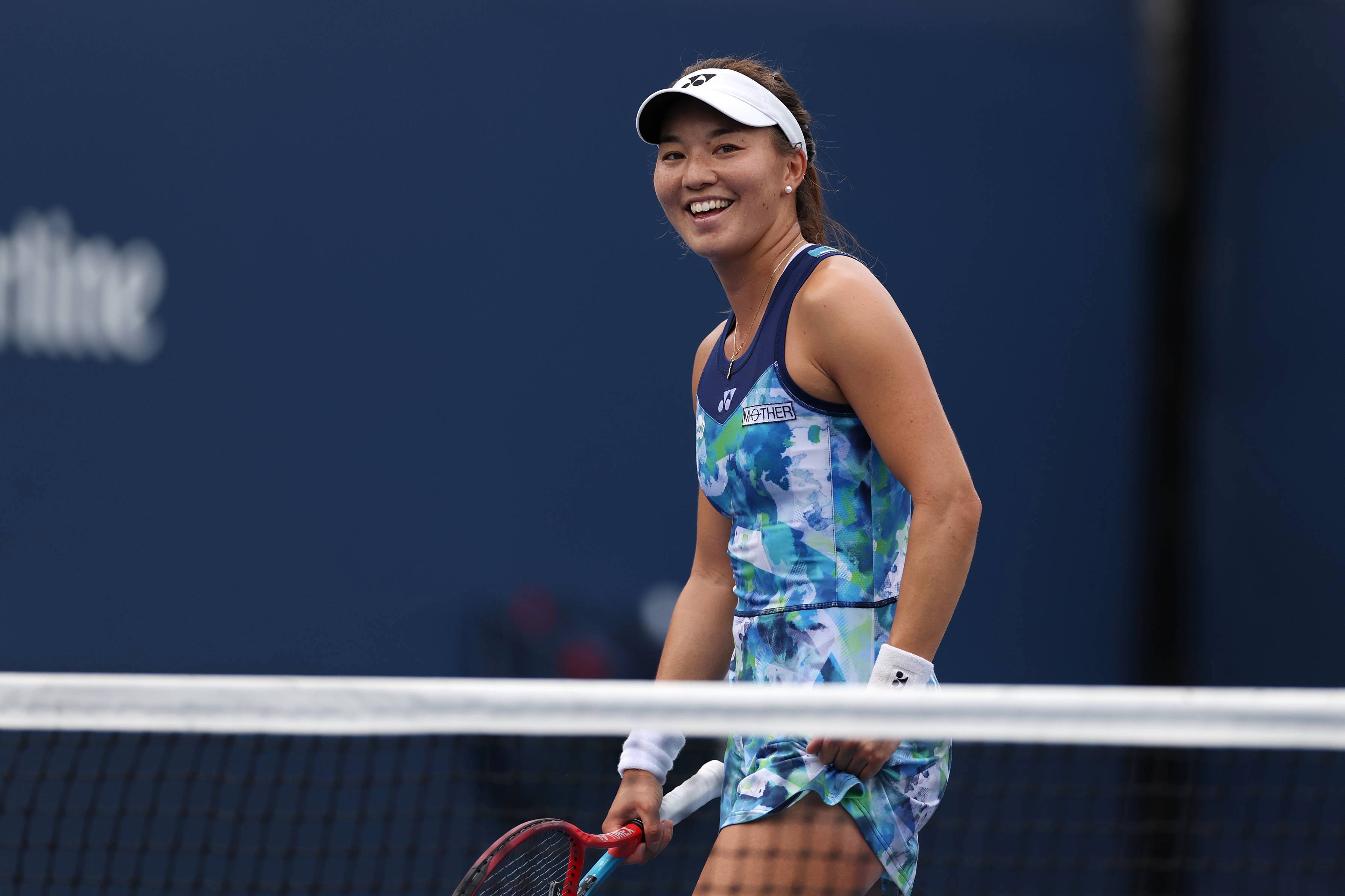 Lily Miyazaki smiling and holding her tennis racket on court at the US Open