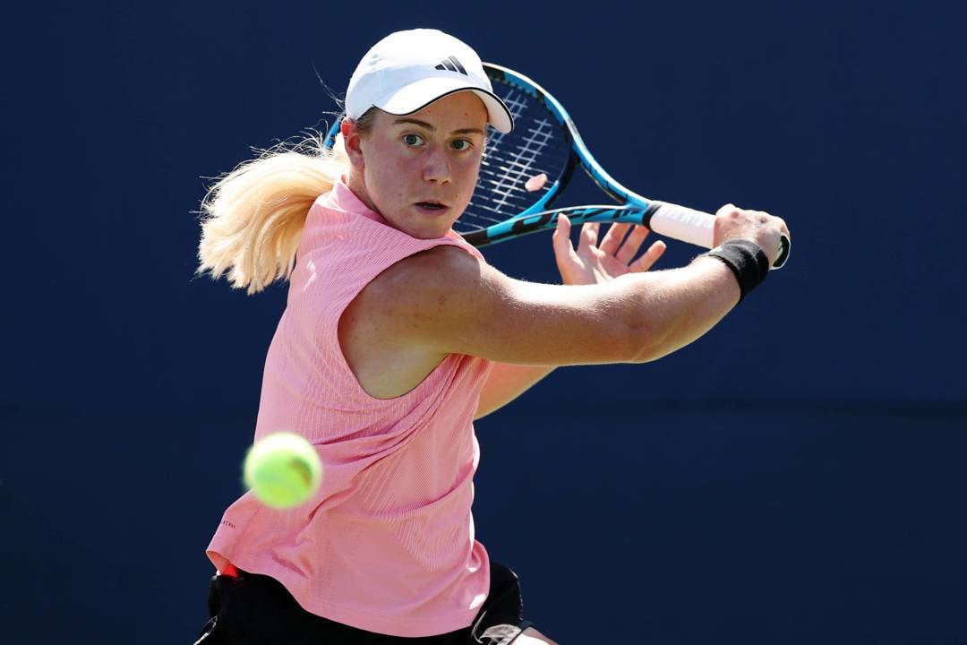 British tennis player Sonay Kartal wearing a pink top with a white Adidas hat while hitting a backhand slice at the US Open