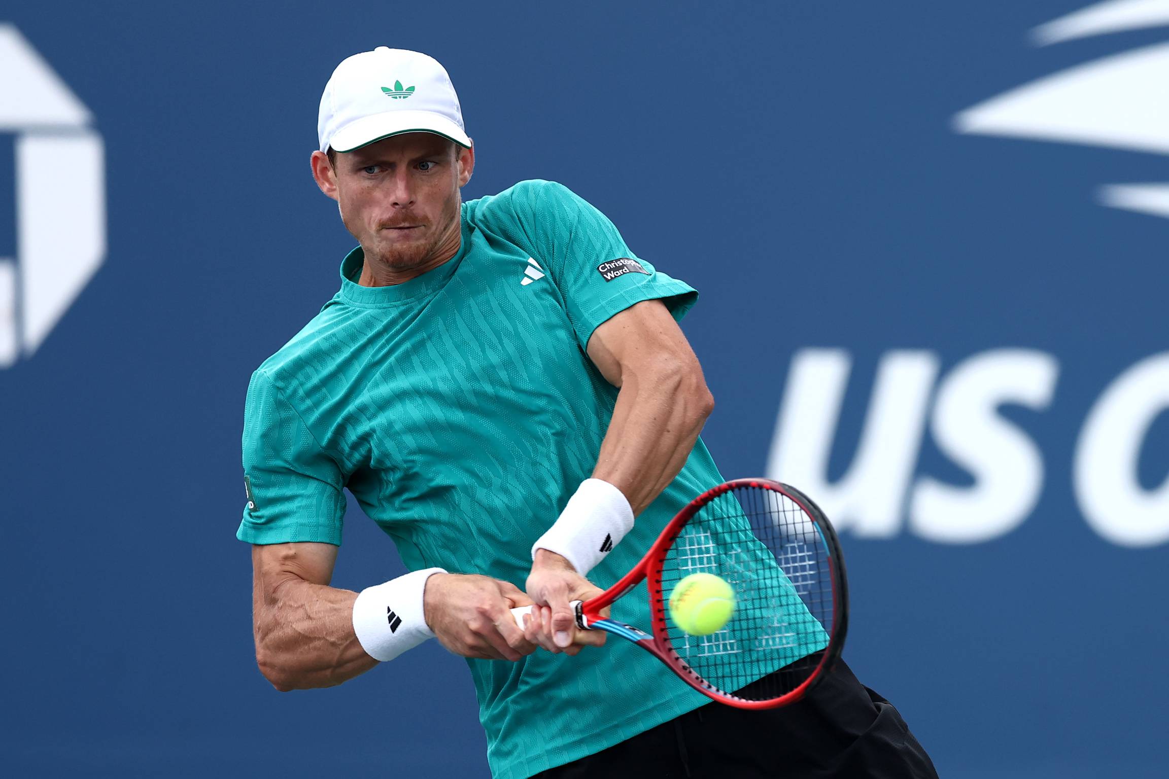 British tennis player Billy Harris wearing a teal Adidas top and hitting a backhand on court at the US Open