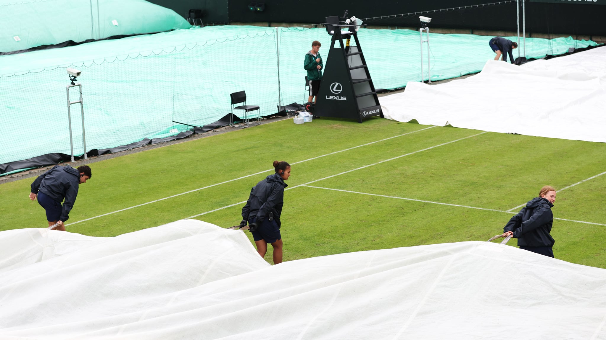 Three grounds staff pull the covers over the court during the rain