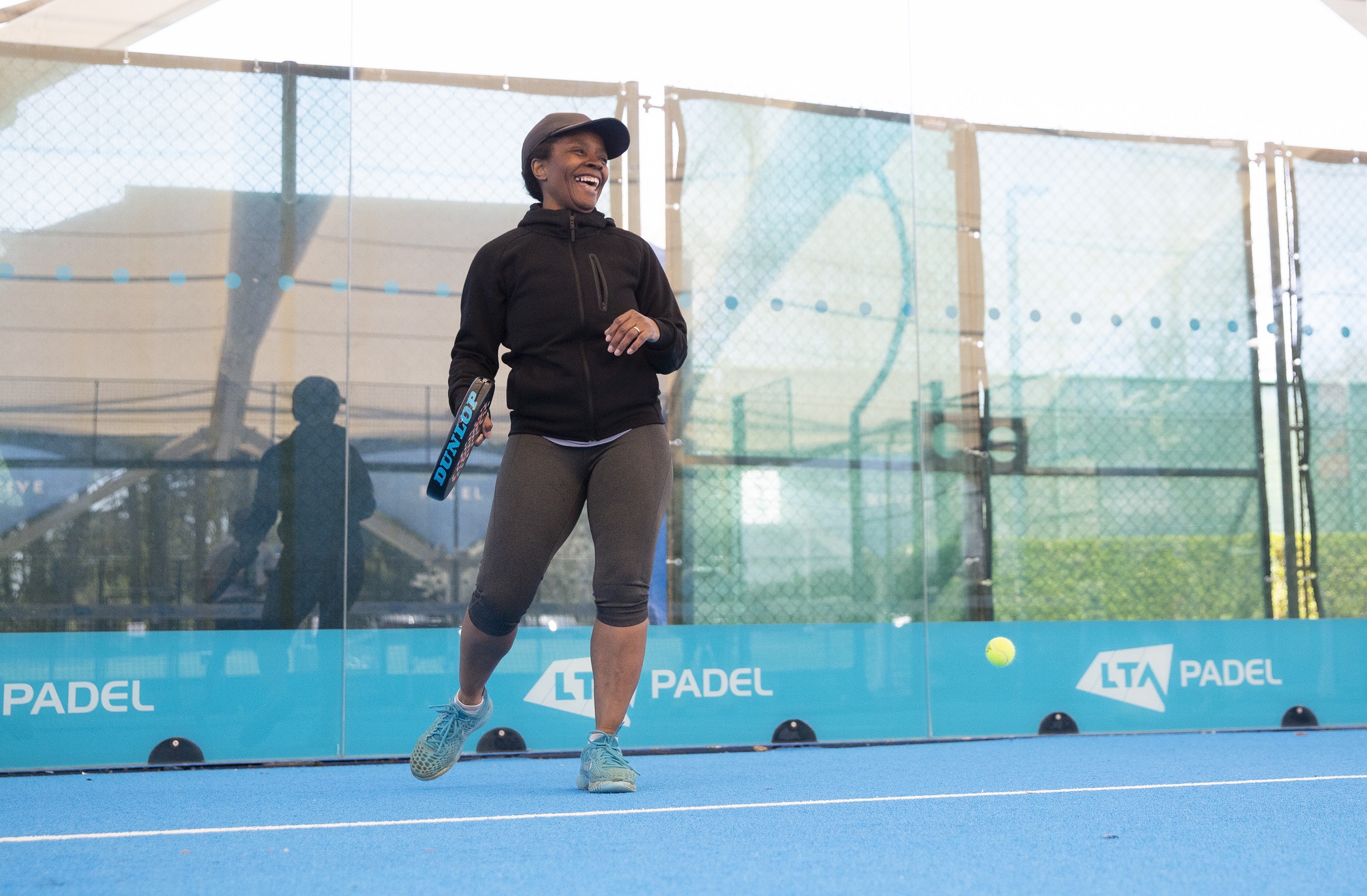 Female player laughing, holding a padel racket and standing in a padel court.jpg