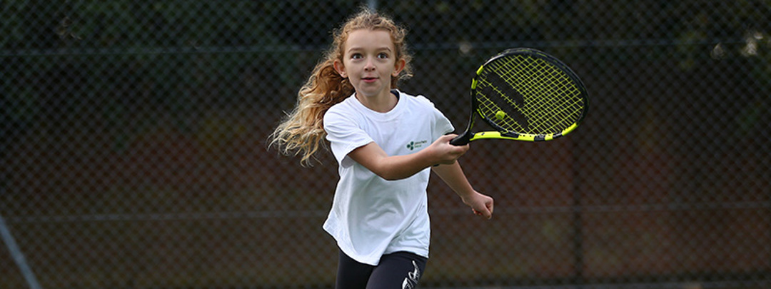 Young girl playing tennis with a black and yellow racket
