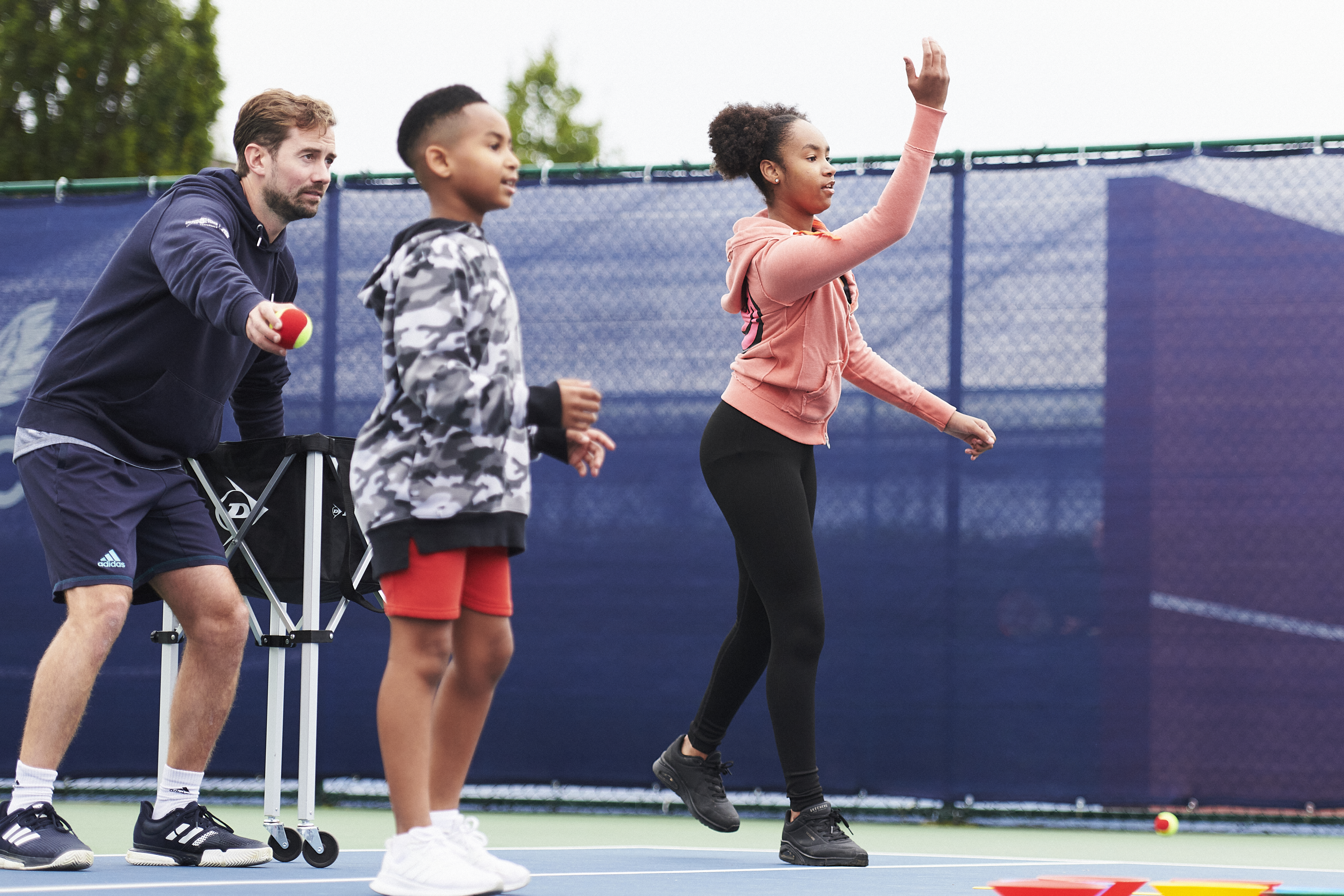 A tennis coach on court with two junior players